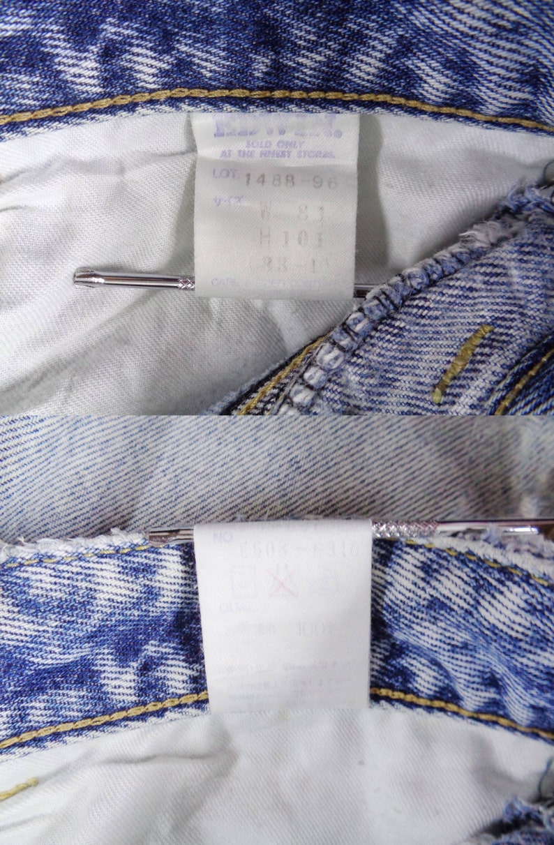 May include: Close-up of the inside of blue denim jeans, showing the white fabric and tags. The tags display text including size information and care instructions. A silver metal pin is holding the fabric together.