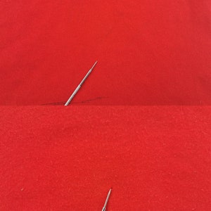 May include: A close-up shot of a silver needle with a textured handle, positioned on a vibrant red fabric. The needle's sharp point is visible, suggesting its use in sewing or embroidery. A dark line is drawn on the fabric.