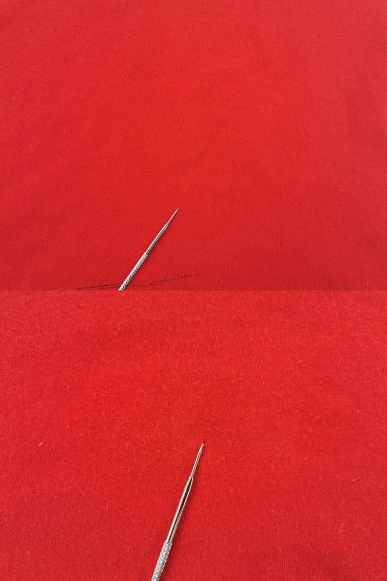 May include: A close-up shot of a silver needle with a textured handle, positioned on a vibrant red fabric. The needle's sharp point is visible, suggesting its use in sewing or embroidery. A dark line is drawn on the fabric.