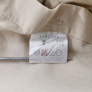 May include: A beige fabric garment tag featuring the text X462109, 85% cotton, and 15% linen, indicated by Japanese characters. The white rectangular label includes four black laundry care symbols, with one symbol marked by a red cross.