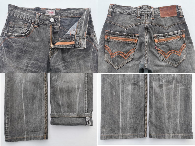 May include: A pair of gray denim jeans with orange stitching and zipper details. The jeans have a classic five-pocket design, a button and zipper closure, and a leather patch on the back. The jeans are folded at the bottom.