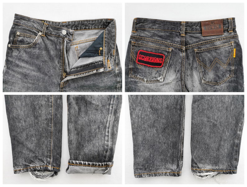 May include: Acid-washed black denim jeans featuring a button fly, a brown leather EDWIN brand patch on the back waistband, and a rectangular patch on the back pocket with the red text SCORPIONS. The jeans have frayed hems and orange stitching.