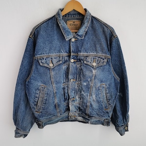 May include: A vintage blue denim jacket with a button-up front, two chest pockets, and two side pockets. The jacket has a classic collar and is hanging on a wooden hanger. The brand tag "Edwin" is visible on the collar.