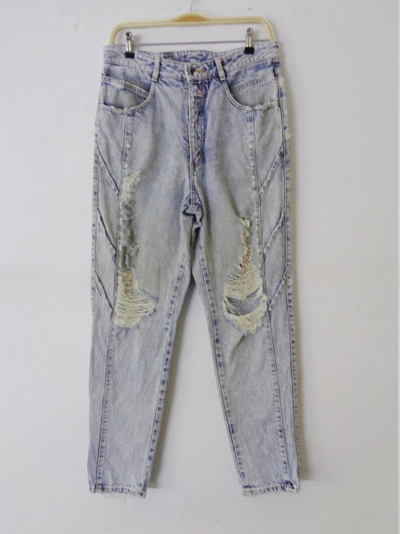 May include: Light blue acid wash jeans with distressed details. The jeans have a high waist, a button and zipper closure, and pockets. The denim pants are hanging on a hanger against a white background.