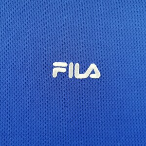 Puede incluir: Primer plano de una camiseta deportiva azul real con tejido texturizado y transpirable. El logotipo blanco "FILA" bordado est&aacute; centrado en el pecho. El dise&ntilde;o de la camiseta sugiere que est&aacute; hecha para deportes o uso casual.