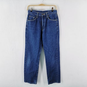 Puede incluir: Un par de vaqueros cl&aacute;sicos azules colgados de una percha de madera. Los vaqueros tienen un corte recto, dise&ntilde;o de cinco bolsillos y cierre de bot&oacute;n y cremallera. El denim tiene un lavado medio con sutiles decoloraciones.