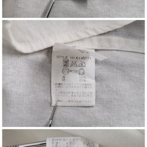 May include: A close-up of a white fabric label with the AVIREX brand logo and washing instructions. The tag displays the style number 6145111 and fabric composition details. The fabric is 55% linen and 45% cotton.