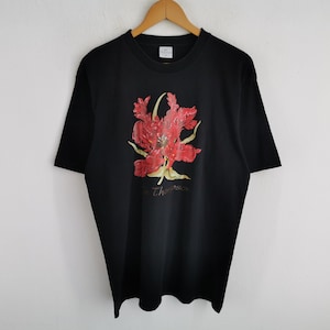 May include: Black t-shirt featuring a vibrant red and yellow floral design. The design includes the name "Thompson" in a cursive font. The shirt is hanging on a wooden hanger against a white background.