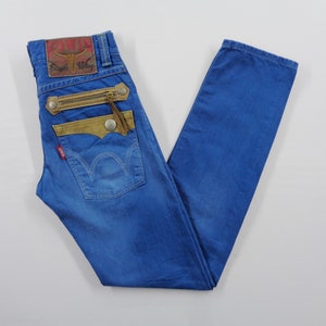 K&ouml;nnte beinhalten: Blaue Jeans aus Denim mit einzigartigen Designelementen. Mit einem braunen Lederaufn&auml;her, einer Rei&szlig;verschlusstasche und einem roten Logo-Etikett. Die Jeans haben ein klassisches F&uuml;nf-Taschen-Design und einen geraden Beinverlauf.