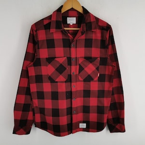 May include: Red and black plaid flannel shirt with two chest pockets. The long-sleeved shirt has a button-down front and a collar. The brand name "SSDD" is visible on a tag near the collar and on the pocket.