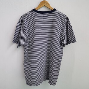 Puede incluir: Camiseta a rayas azul marino y blanca de manga corta, colgada de una percha de madera. La camiseta tiene cuello redondo azul marino. Las rayas horizontales son uniformes en todo el tejido.