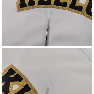 May include: Close-up of a white fabric with the word "HELLO KITTY" in black letters with gold glitter trim. A silver tool is in the image.
