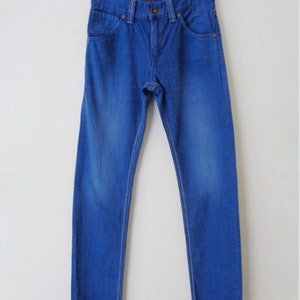 K&ouml;nnte beinhalten: Hellblaue Jeans aus Denim, die an einem Kleiderb&uuml;gel h&auml;ngen. Die Jeans haben ein klassisches F&uuml;nf-Taschen-Design mit Knopf- und Rei&szlig;verschluss. Die N&auml;hte sind wei&szlig;, und der Denim hat ein leicht verwaschenes Aussehen.