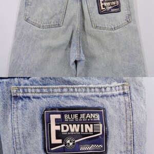 May include: Light blue denim jeans with a faded wash. The back features two pockets and a black leather patch detail at the waistband. A rectangular patch on the back pocket reads "BLUE JEANS" and "EDWIN".