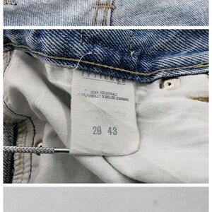 May include: Close-up of light blue denim jeans with a Versace Jeans Couture label. The jeans have a faded wash and visible stitching. The interior tag shows size 29 and 43. The care label is also visible.