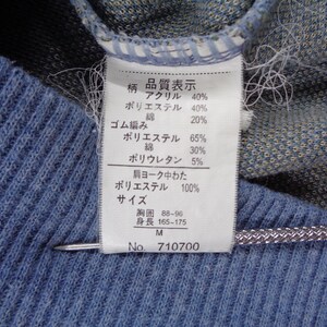 Puede incluir: Primer plano de una tela de punto azul con una etiqueta blanca adjunta. La etiqueta muestra texto japon&eacute;s con porcentajes de composici&oacute;n de la tela, incluyendo acr&iacute;lico, poli&eacute;ster y algod&oacute;n. La etiqueta tambi&eacute;n incluye la talla, la medida del pecho y un n&uacute;mero de producto.