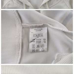 May include: White zip-up hoodie with gold glitter "HELLO KITTY" lettering on the hood. The hood lining features a leopard print. The hoodie has gold stripes on the sleeves and a "Hello Kitty" label.