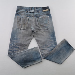 K&ouml;nnte beinhalten: Hellblaue Jeans mit verwaschener Optik und Used-Details. Die Jeans haben ein klassisches F&uuml;nf-Taschen-Design, einen Knopf- und Rei&szlig;verschluss und einen Lederaufn&auml;her auf der R&uuml;ckseite. Die Jeans liegen flach auf einer wei&szlig;en Oberfl&auml;che.