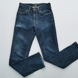 May include: Dark blue denim jeans with a classic five-pocket design. The jeans have a button and zipper closure, belt loops, and a faded wash. The Wrangler logo is visible on the back pocket. A timeless wardrobe staple.