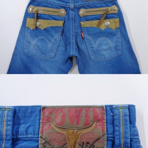 K&ouml;nnte beinhalten: Blaue Jeans aus Denim mit einzigartigen Designelementen. Sie verf&uuml;gen &uuml;ber beigefarbene Akzente, dekorative Rei&szlig;verschl&uuml;sse und einen Lederaufn&auml;her mit einem Bullenkopf-Logo. Die Jeans haben ein klassisches F&uuml;nf-Taschen-Design.