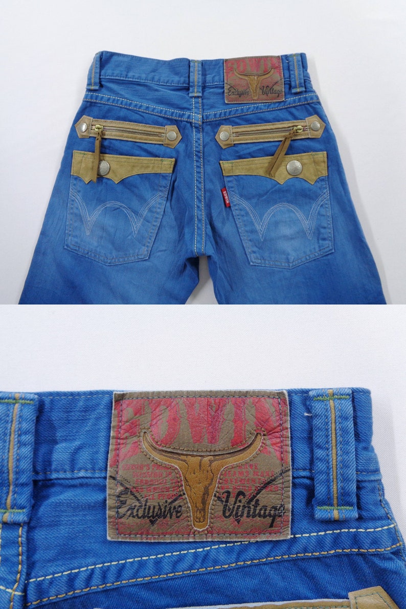 K&ouml;nnte beinhalten: Blaue Jeans aus Denim mit einzigartigen Designelementen. Sie verf&uuml;gen &uuml;ber beigefarbene Akzente, dekorative Rei&szlig;verschl&uuml;sse und einen Lederaufn&auml;her mit einem Bullenkopf-Logo. Die Jeans haben ein klassisches F&uuml;nf-Taschen-Design.