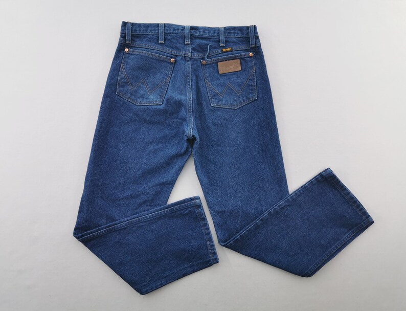 K&ouml;nnte beinhalten: Blaue Jeans aus Denim mit klassischem F&uuml;nf-Taschen-Design. Die Jeans haben Kupfernieten, einen braunen Lederaufn&auml;her und das Wrangler-Logo. Die Jeans sind im Straight-Leg-Stil.