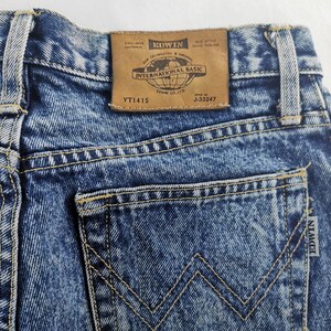 Puede incluir: Primer plano de unos vaqueros de mezclilla azules con un lavado descolorido. Los bolsillos traseros presentan un dise&ntilde;o distintivo y la etiqueta de la marca "EDWIN INTERNATIONAL BASIC" es visible. Los vaqueros tienen una est&eacute;tica cl&aacute;sica y vintage.
