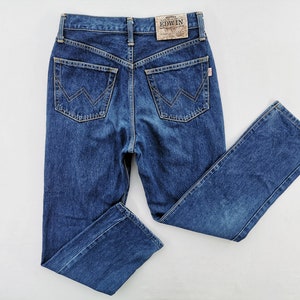 Puede incluir: Vaqueros de mezclilla azul oscuro con un dise&ntilde;o cl&aacute;sico de cinco bolsillos. Presentan cintura alta, pernera recta y el nombre de la marca "EDWIN" en un parche de cuero. Los bolsillos traseros tienen una costura distintiva en forma de W.