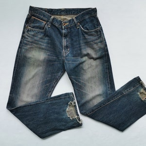 Pu&ograve; includere: Jeans in denim blu sbiadito con dettagli distressed. I jeans hanno un classico design a cinque tasche, una chiusura con bottone e cerniera e un aspetto usurato. Gli orli sono sfilacciati, aggiungendo all'estetica vintage. Un capo casual.