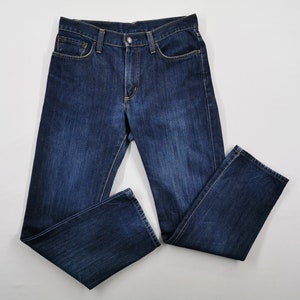 May include: Dark blue denim jeans with a classic five-pocket design. The jeans are laid flat, showcasing the front and back pockets, belt loops, and button closure. The fabric has a slightly faded appearance.