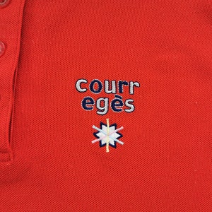 K&ouml;nnte beinhalten: Ein rotes Poloshirt mit drei transparenten Kn&ouml;pfen und einem Kragen. Auf dem Shirt ist der Text "COURR eges" in Wei&szlig; und Marineblau sowie ein kleines, farbenfrohes Emblem gestickt.