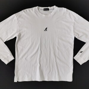 Op de afbeelding: Wit shirt met lange mouwen en een ronde hals. Het shirt heeft een klein zwart kangoeroe-logo op de borst en een bijpassend logo op de linker manchet. De merknaam is in het zwart rond de kraag gedrukt.