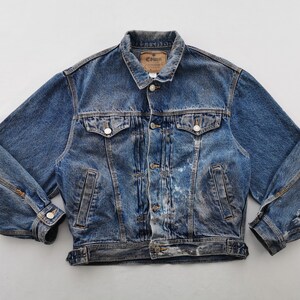 May include: A vintage blue denim jacket with a button-down front, two chest pockets, and two side pockets. The jacket has a classic collar and a distressed look with some wear and tear. The brand label "Edwin" is visible on the collar.