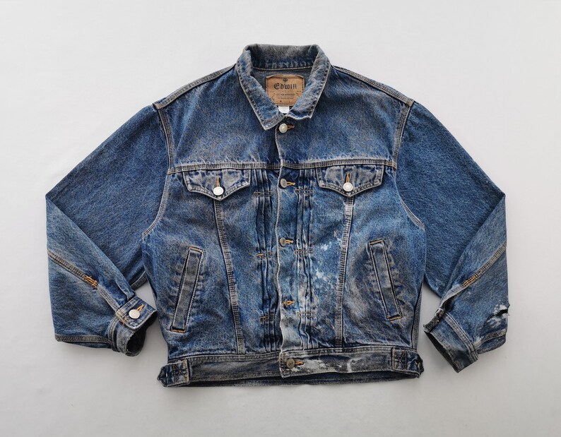 May include: A vintage blue denim jacket with a button-down front, two chest pockets, and two side pockets. The jacket has a classic collar and a distressed look with some wear and tear. The brand label "Edwin" is visible on the collar.