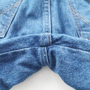 K&ouml;nnte beinhalten: Nahaufnahme einer blauen Jeans. Das Bild zeigt die Ges&auml;&szlig;taschen, N&auml;hte und den Taillenbereich. Die N&auml;hte sind in einer kontrastierenden beigen Farbe gehalten. Der Denim hat einen klassischen, abgenutzten Look.