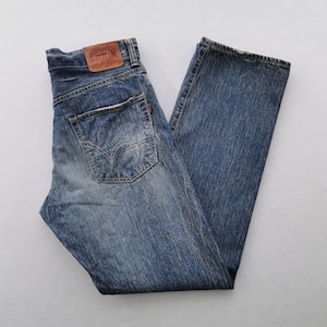 May include: Blue denim jeans with a faded wash. The jeans have a classic five-pocket design, a brown leather patch, and a straight leg. The jeans are folded neatly on a white surface.