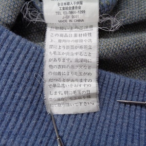 Puede incluir: Primer plano de una tela de punto azul con una etiqueta adjunta. La etiqueta tiene texto japon&eacute;s y una peque&ntilde;a cantidad de texto en ingl&eacute;s. La tela tiene una textura acanalada y es de color azul claro.