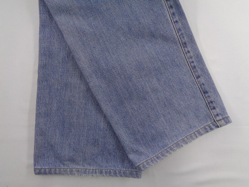 May include: Light blue denim jeans, folded and displayed. The fabric shows a classic denim texture with visible stitching along the seams. The jeans are a medium wash, suitable for casual wear.