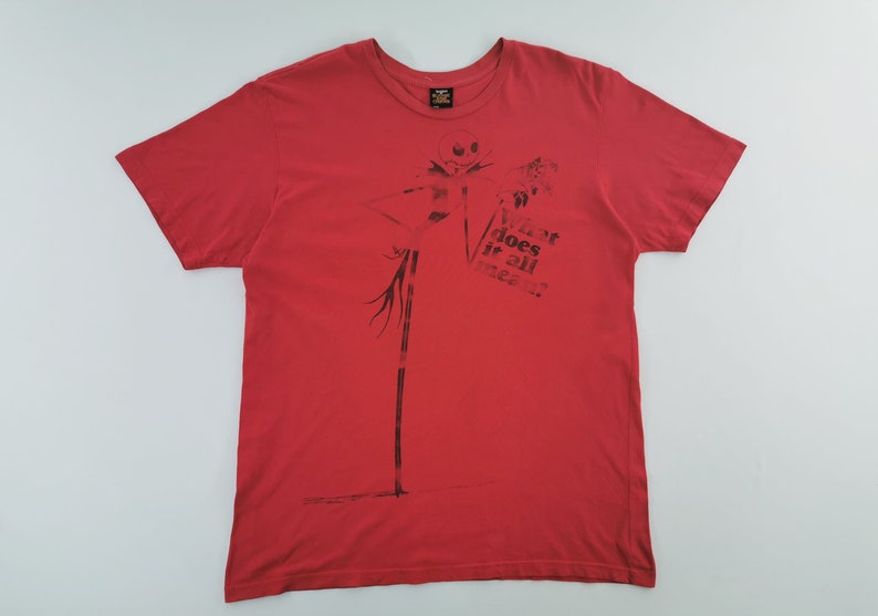 May include: Red t-shirt featuring a black graphic of Jack Skellington from The Nightmare Before Christmas. The shirt also has the text "What does it all mean?" printed on the front.