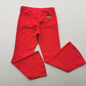 May include: Bright red Wrangler pants with a flared leg design. The pants have two back pockets and a small Wrangler label. The pants are made of a durable fabric and are likely vintage.