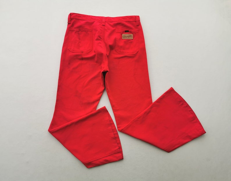 May include: Bright red Wrangler pants with a flared leg design. The pants have two back pockets and a small Wrangler label. The pants are made of a durable fabric and are likely vintage.