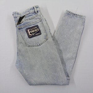 May include: Light blue acid wash denim jeans with a straight leg cut. The jeans feature a back pocket with a black and blue Edwin patch. The jeans are laid flat on a white surface.