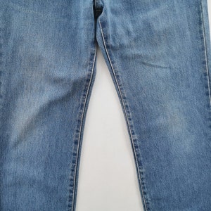 Puede incluir: Vaqueros de mezclilla azul claro. Los vaqueros tienen un dise&ntilde;o cl&aacute;sico de cinco bolsillos y un corte recto. La mezclilla tiene un aspecto descolorido, con &aacute;reas m&aacute;s claras en los muslos y las rodillas.
