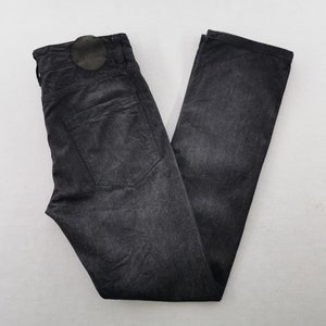 May include: A pair of dark gray denim jeans, folded neatly. The jeans have a classic five-pocket design, a button and zipper closure, and a leather patch on the back. The fabric has a slightly faded, textured appearance.