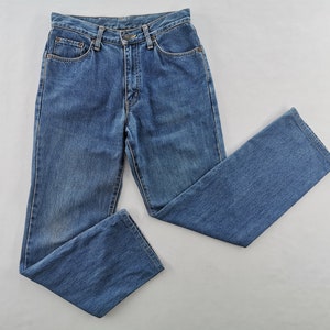 Puede incluir: Un par de vaqueros de mezclilla azules, con un dise&ntilde;o cl&aacute;sico de cinco bolsillos y corte recto. Los vaqueros est&aacute;n hechos de una tela de mezclilla de lavado medio y tienen cierre de bot&oacute;n y cremallera. Los vaqueros est&aacute;n planos sobre una superficie blanca.