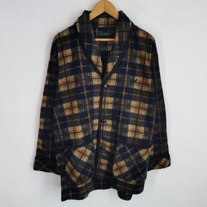 Puede incluir: Chaqueta vintage con botones y estampado de cuadros en azul marino, marr&oacute;n y beige. La chaqueta tiene cuello chal, dos bolsillos delanteros y un peque&ntilde;o logotipo en el pecho. Cuelga de una percha de madera.