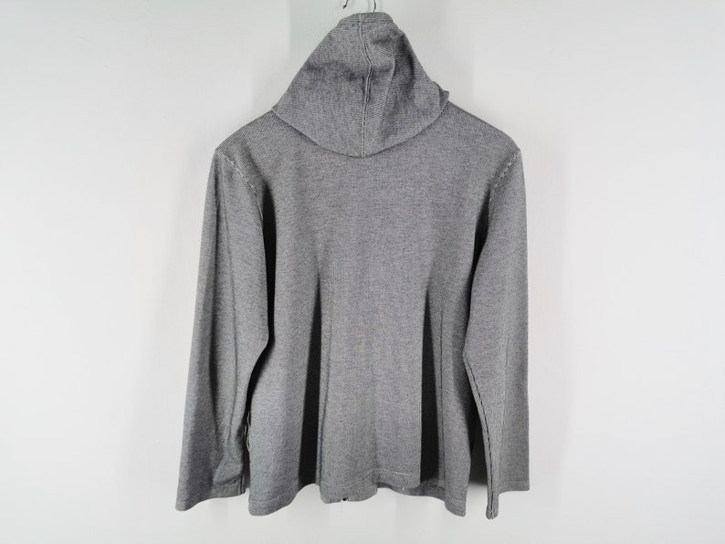 May include: A long-sleeved gray hooded sweatshirt featuring a textured knit fabric. The garment includes a hood at the neckline and long sleeves, with a straight hemline at the bottom. The overall design is simple, featuring a consistent gray color.