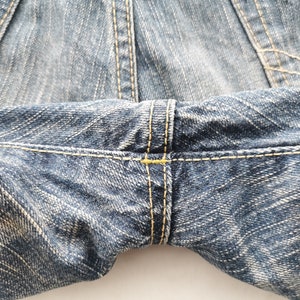 May include: Close-up of blue denim jeans, showcasing the texture and stitching details. The image highlights the seams and the fabric's weave, with yellow thread used for the stitching.