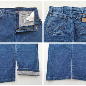 K&ouml;nnte beinhalten: Blaue Jeans aus Denim mit klassischem F&uuml;nf-Taschen-Design. Die Jeans haben einen Knopf- und Rei&szlig;verschluss, G&uuml;rtelschlaufen und das Wrangler-Markenetikett auf der Ges&auml;&szlig;tasche. Die Jeans werden aus verschiedenen Blickwinkeln gezeigt.