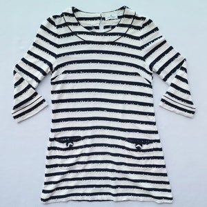 Puede incluir: Vestido color crema con rayas horizontales azul marino. Tiene mangas tres cuartos, cuello redondo y dos peque&ntilde;os bolsillos con detalles de lazo. El vestido mide aproximadamente 86 cm de largo.